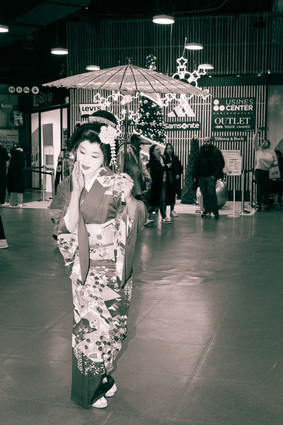Geisha sous une ombrelle traditionnelle dans les allées du centre commercial