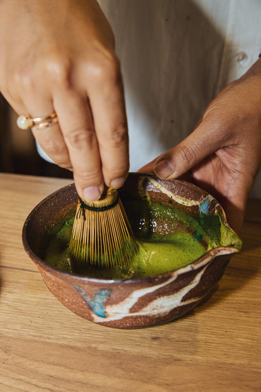 Hands whisking matcha in a rustic bowl